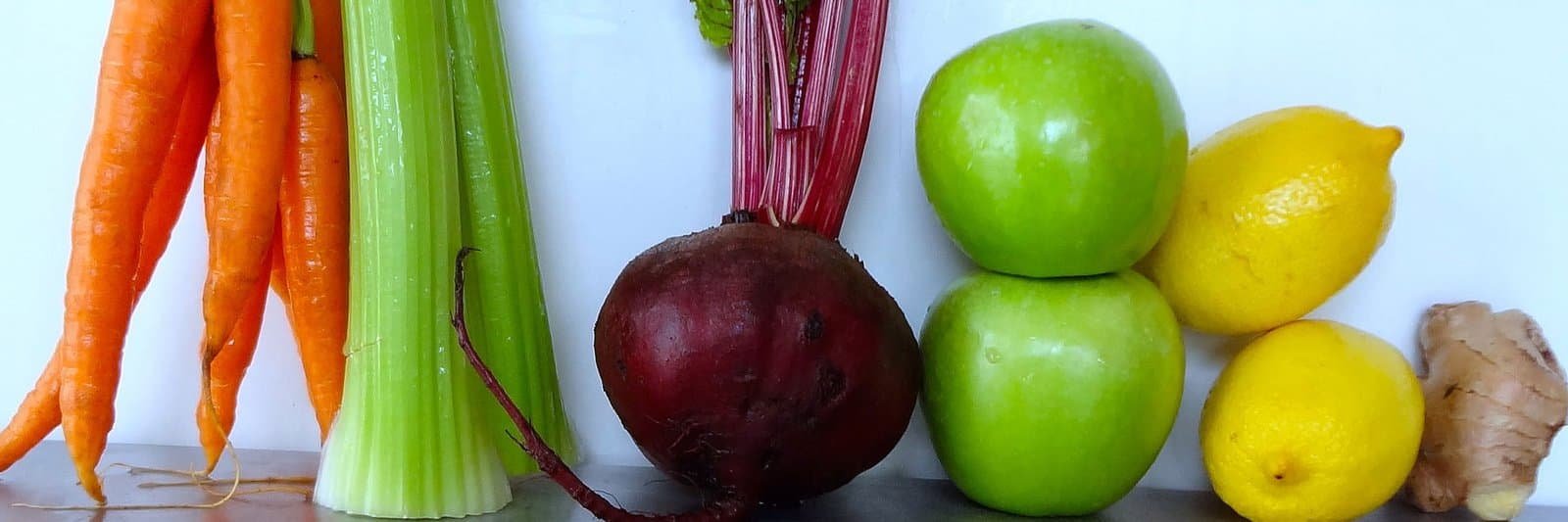 Assorted fresh vegetables and fruits including carrots, celery, beetroot, apples, lemon, and ginger.