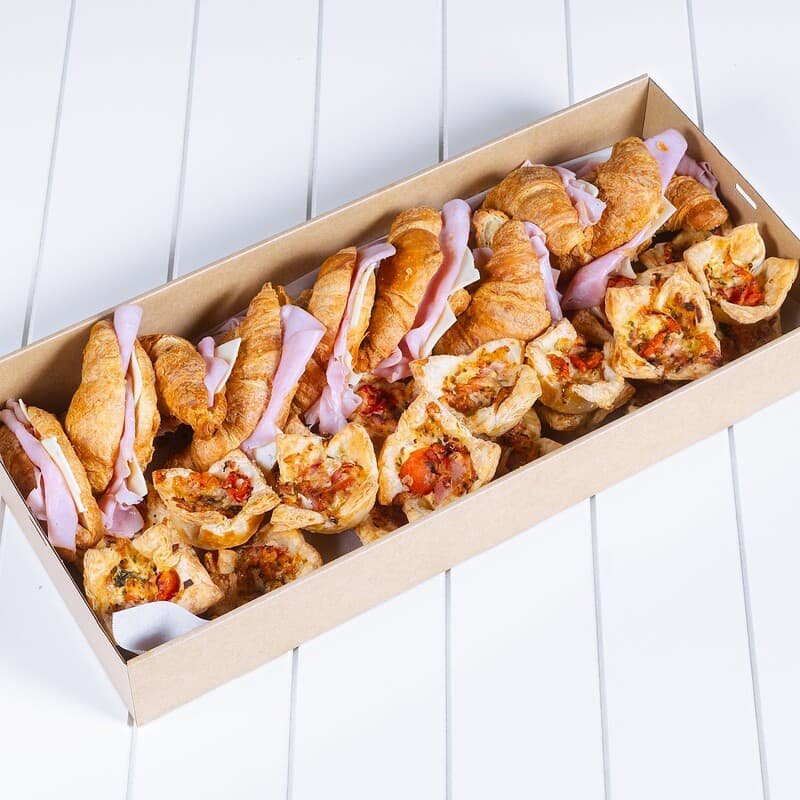 Assorted mini pizzas with toppings in a rectangular box on a white surface.