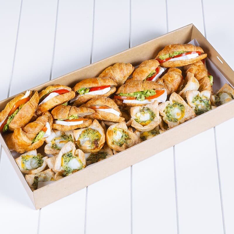 Assorted gourmet sandwiches and wraps in a cardboard box on a white surface.