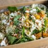 Fresh green salad with roasted pumpkin, nuts, and cheese in a wooden box.