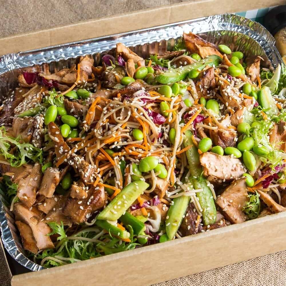 Fresh Asian-style noodle salad with vegetables and sesame seeds in a foil tray.