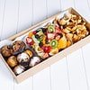 Assorted fresh fruit, muffins, and pastries in a box on a white surface.