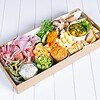 Gourmet charcuterie board with cheeses, meats, vegetables, and dips on a white surface.