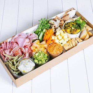 Gourmet charcuterie board with cheeses, meats, vegetables, and dips on a white surface.