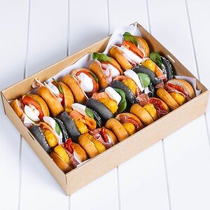 Assorted mini hot dogs in a cardboard tray on a white surface.