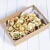 Mini pastry bites with green pesto and melted cheese in a cardboard box.