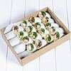 Freshly made wraps with vegetables and meats in a box on a white surface.