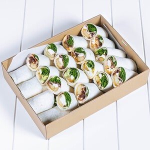 Freshly made wraps with vegetables and meats in a box on a white surface.