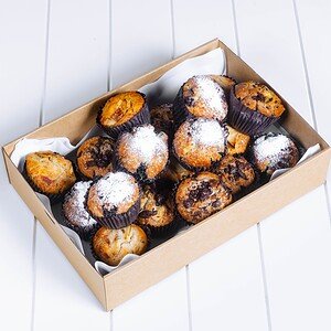 Freshly baked muffins in a cardboard box with powdered sugar on top.