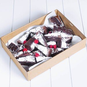 Chocolate brownies with raspberries and powdered sugar in a cardboard tray.