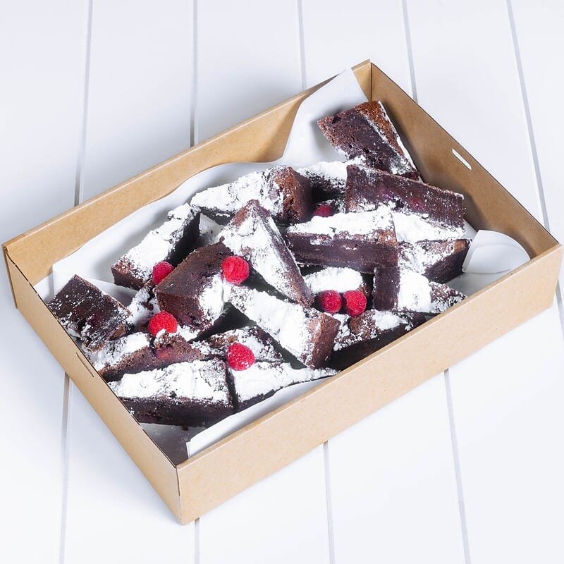 Chocolate brownies with raspberries and powdered sugar in a cardboard tray.