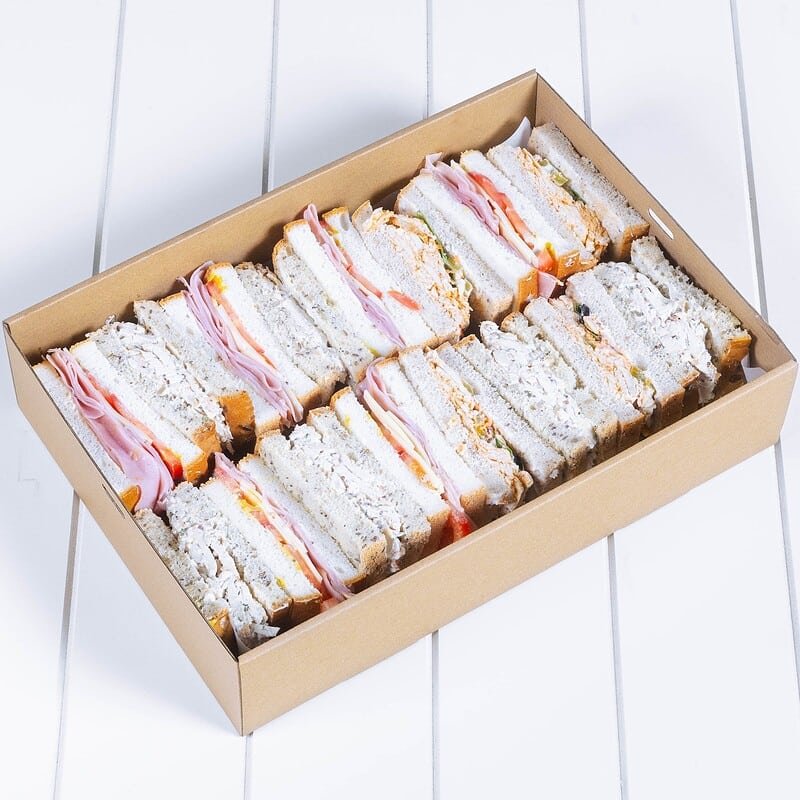 Assorted sandwiches with ham, cheese, and vegetables in a cardboard box.