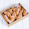 Box of croissant sandwiches with ham and cheese on white surface.