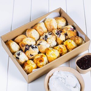 Variety of freshly baked scones with jam and cream on a white table.