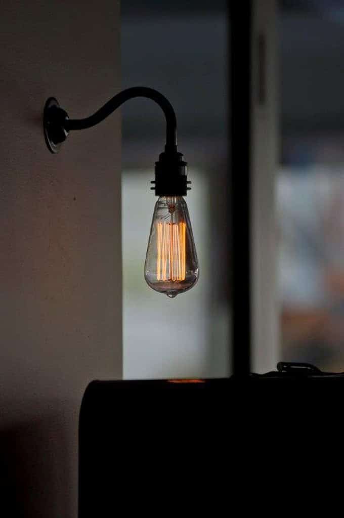 Edison style filament light bulb hanging on wall in dimly lit room.