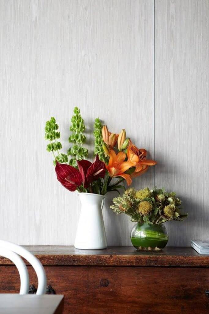 Beautiful flower vases with vibrant lilies and greenery on wooden table.