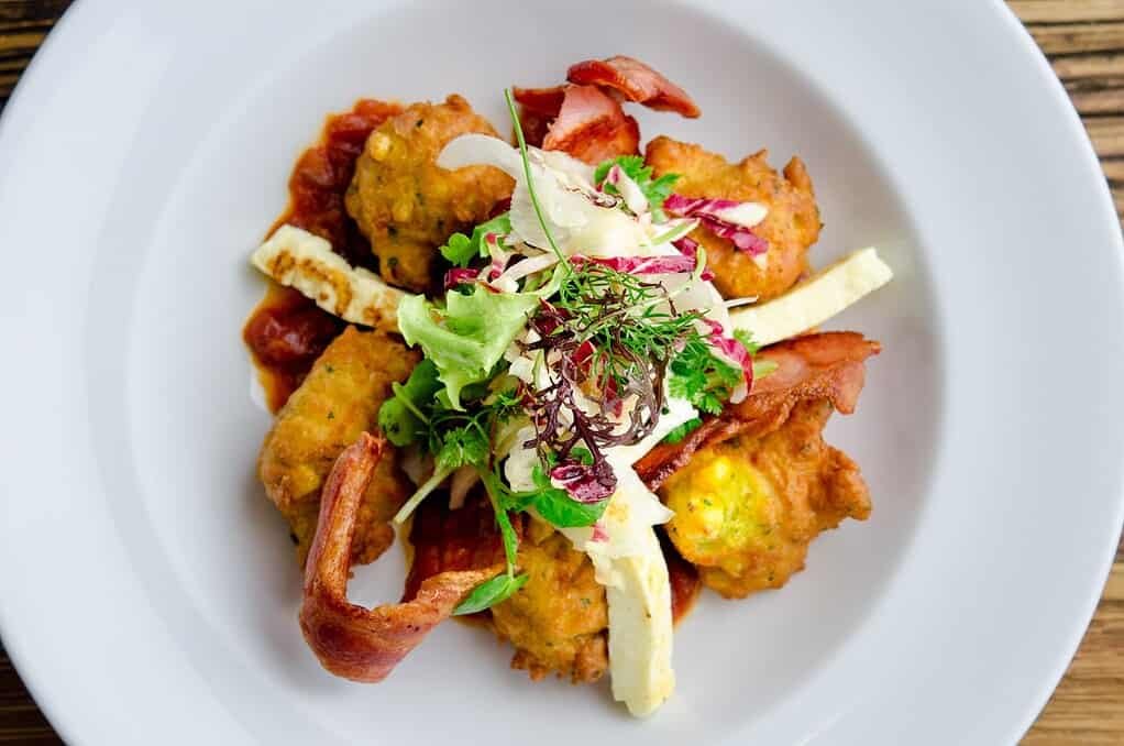 Delicious fried corn fitters with bacon and fresh greens on a white plate.