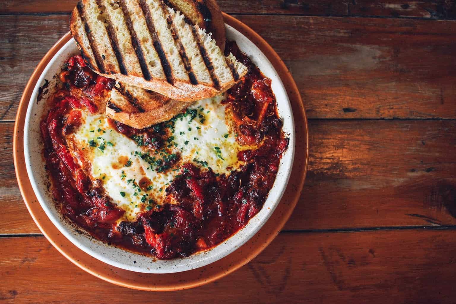 Bowl of delicious oven baked eggs and shakshuka with char-grilled toast