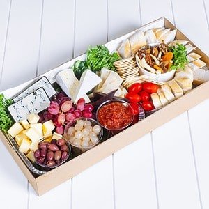 Assorted cheeses, grapes, cherry tomatoes, and cured meats on a cheese board.
