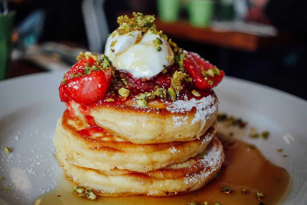Stack of fluffy pancakes topped with strawberries, ice cream, and crushed pistachios.