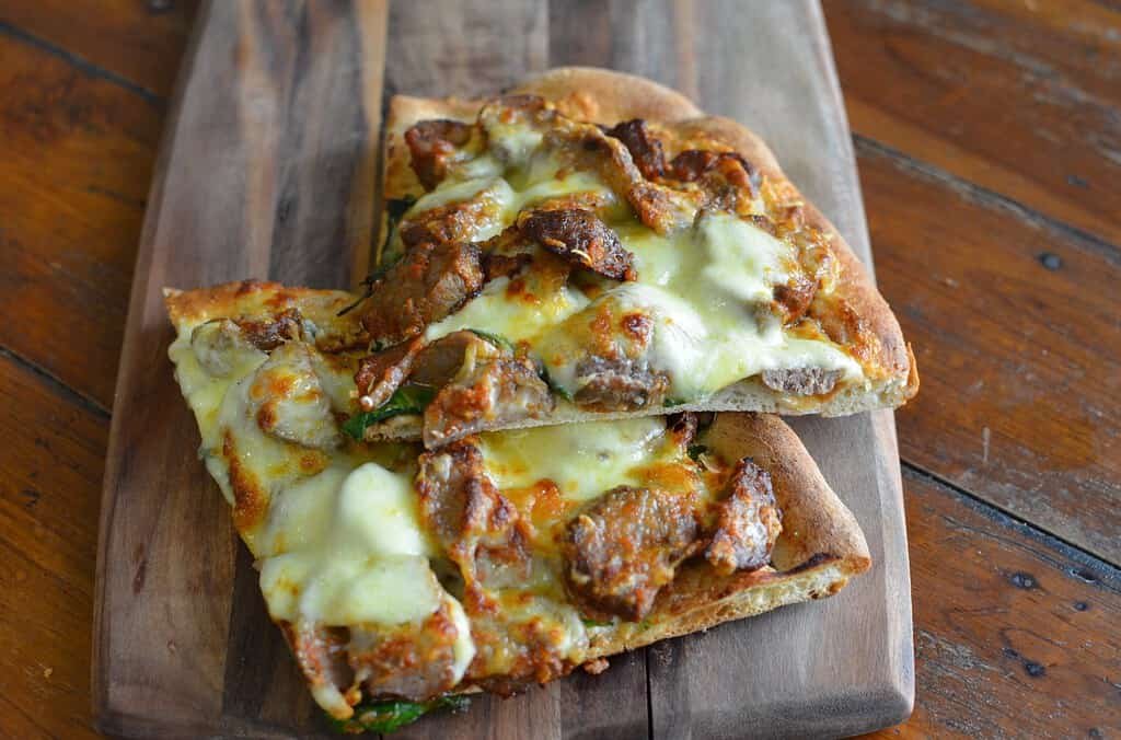 Delicious homemade pizza with cheese and meat toppings on a wooden board.